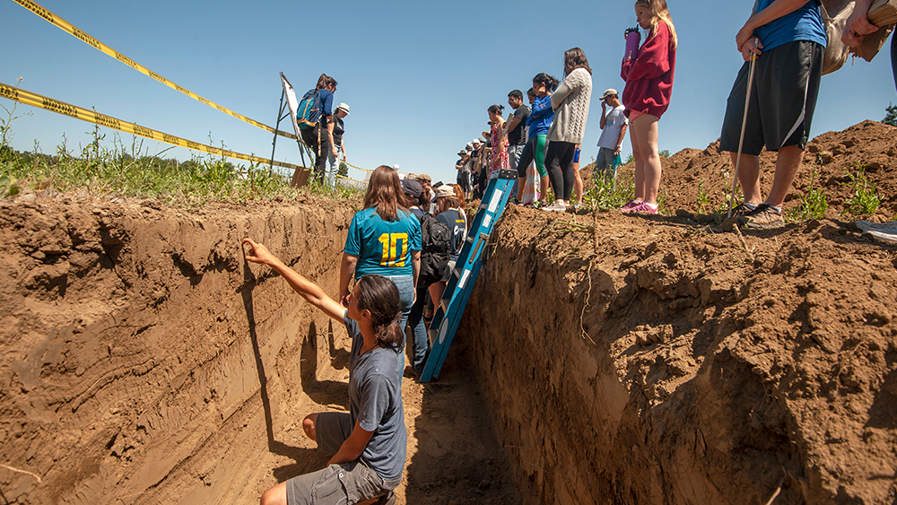 Assistant professor Amelie Gaudin (upper left, white hat) and teaching assistant Cynthia Creze (upper left, blue shirt), a Ph.D. candidate, talk to students about the differences in the striations in the soil as student study it from a four-foot trench during an agroecosystems class. (Gregory Urquiaga/UC Davis)