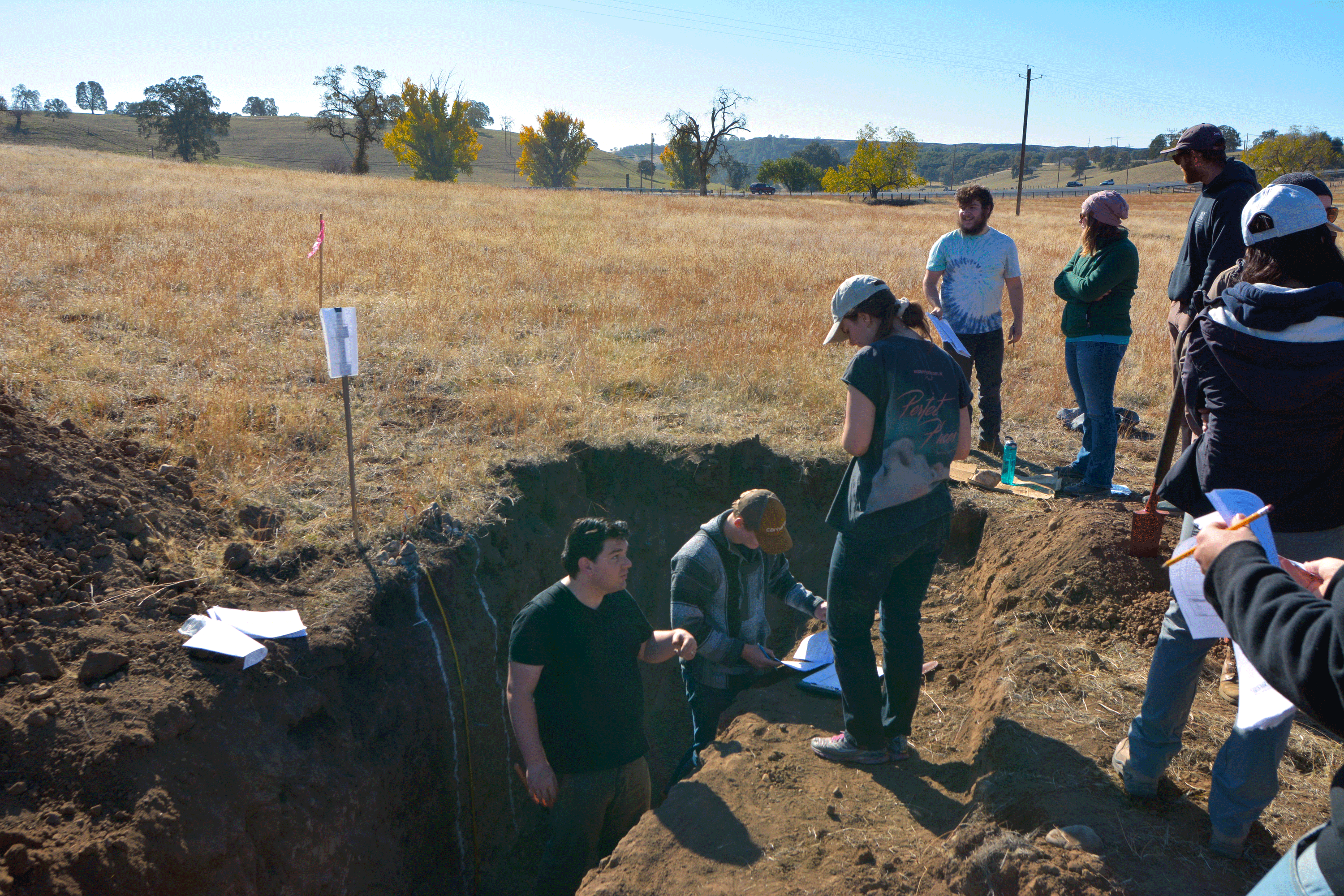 A student stands in a trench while other students observe.